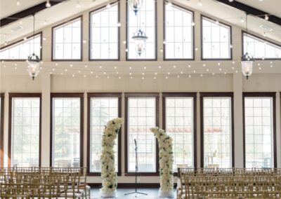 Indoor wedding ceremony setup in the grand ballroom at Running Deer Golf Club with floral arches and string lights