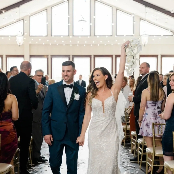 Bride and groom walking up the aisle in the grand ballroom at Running Deer Golf Club surrounded by cheering guests