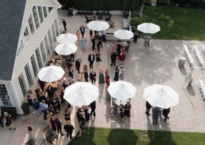 Aerial photo of wedding guests mingling on the patio with white umbrellas next to the clubhouse at Running Deer Golf Club