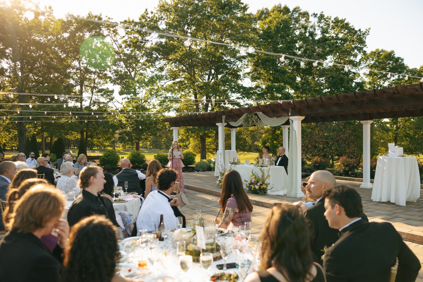 Wedding guests at an outdoor cocktail hour near the pergola at Running Deer Golf Club